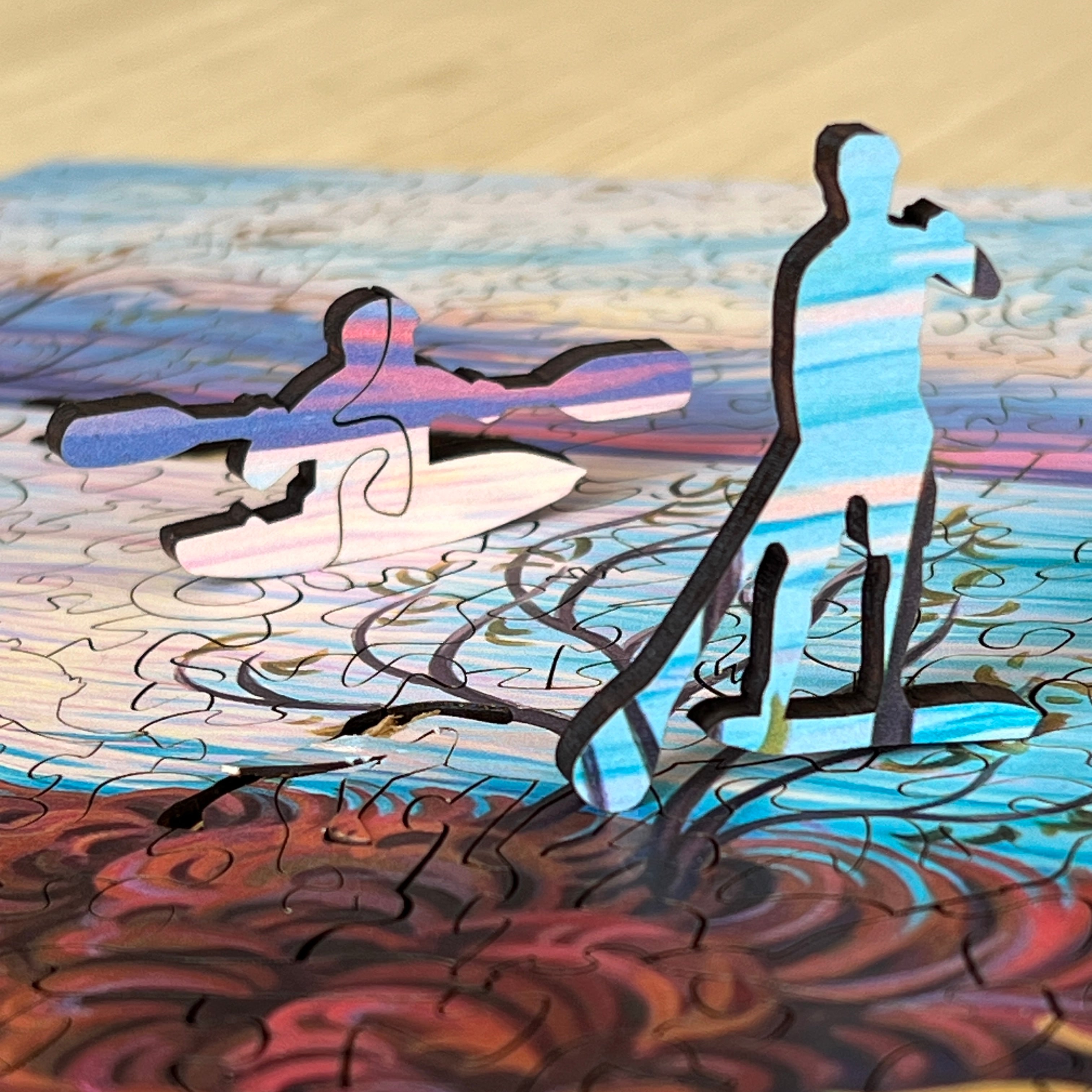 Two wooden jigsaw puzzle whimsy pieces standing up. A kayaker and a paddleboarder.