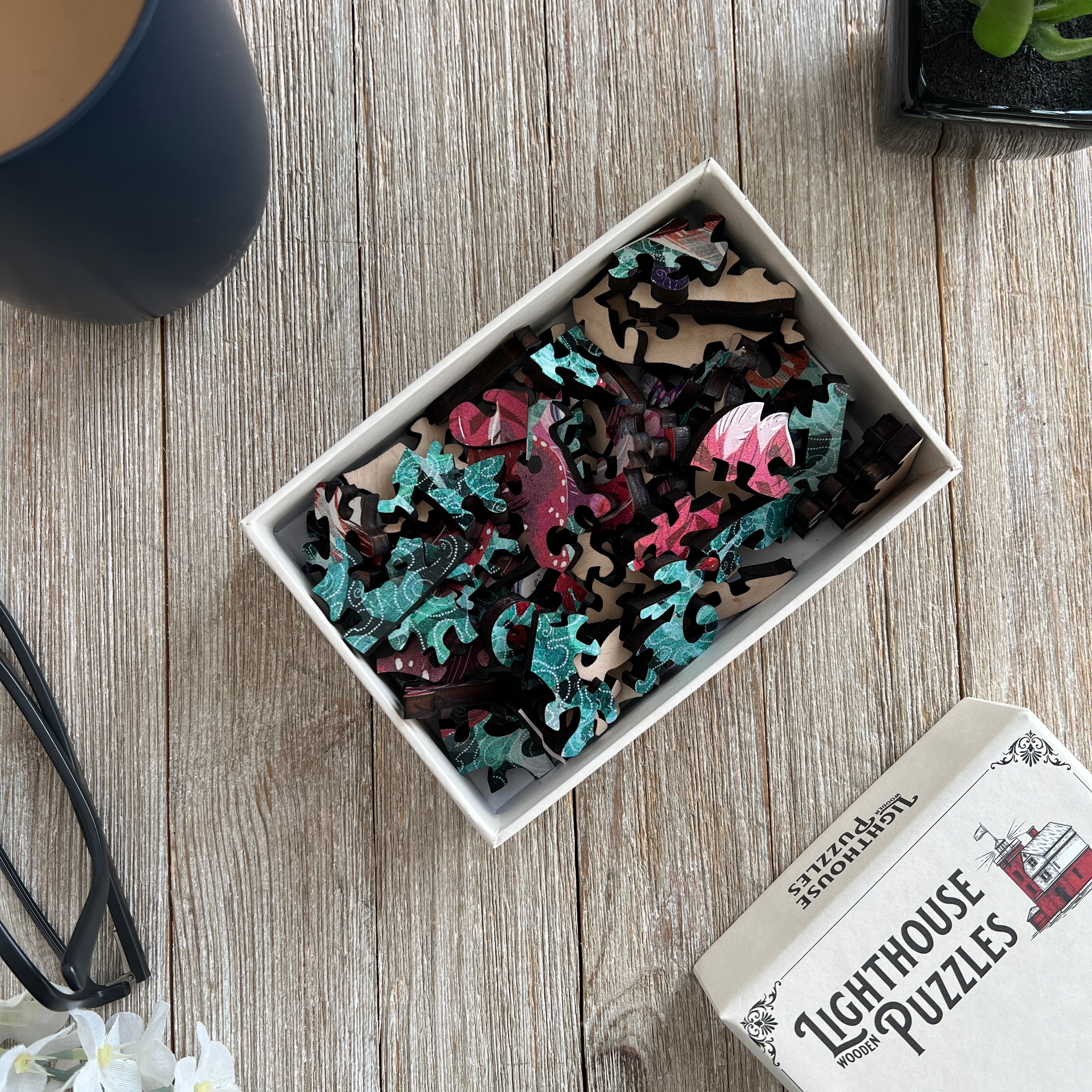 An open box sitting on a table containing wooden jigsaw pieces.